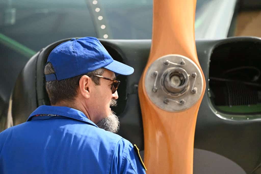 A man in blue shirt and hat looking at a propeller